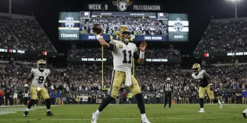 NFL quarterback throwing football during a night game in the 2025 season, with stadium lights and scoreboard visible.